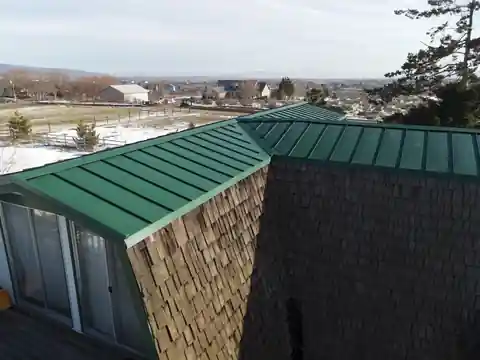 Green standing-seam metal roof on a cedar-shake house with snow in the valley behind