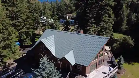 Drone view of the same log home re-roofed in grey standing-seam metal